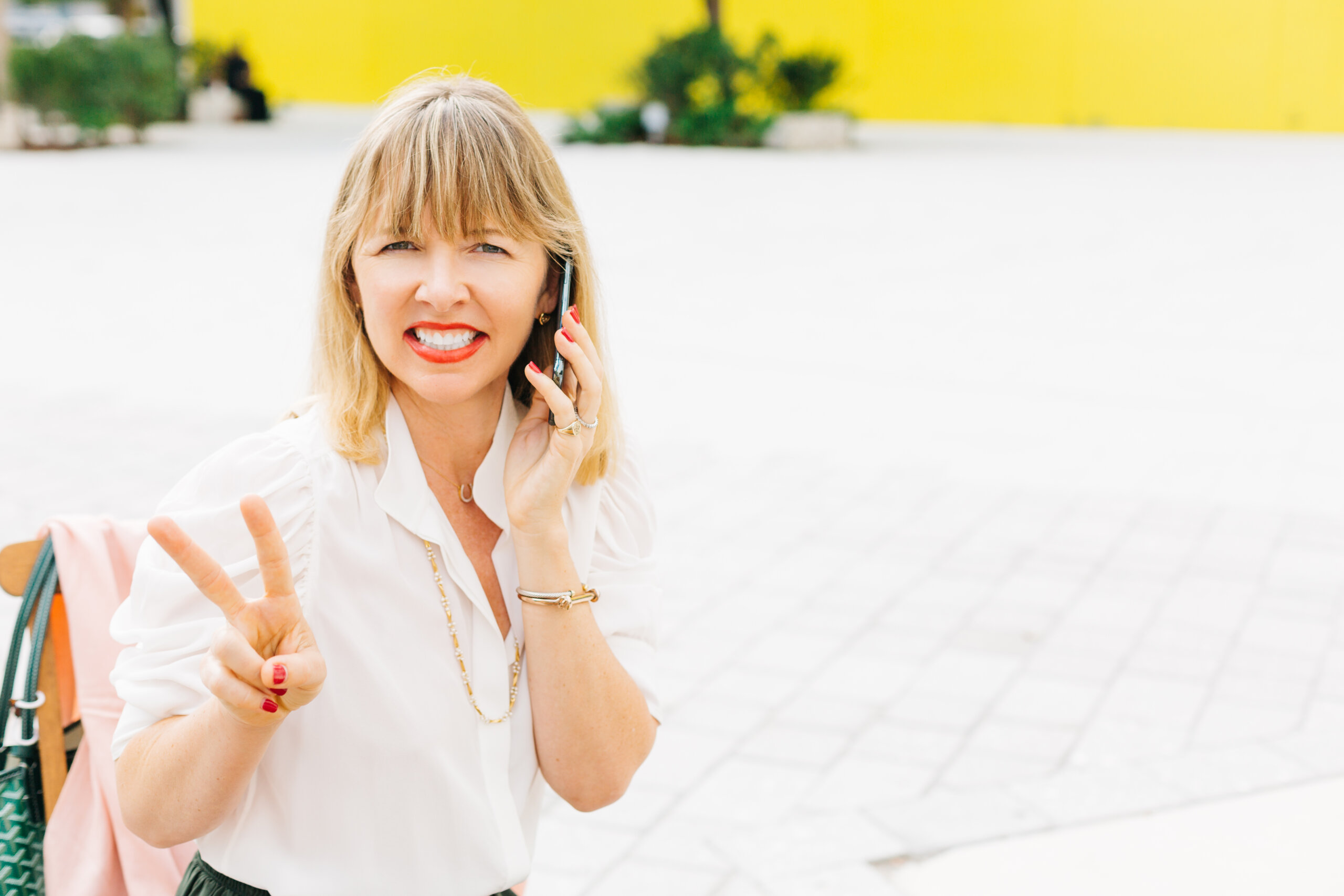 Woman on phone smiling with peace sign fingers